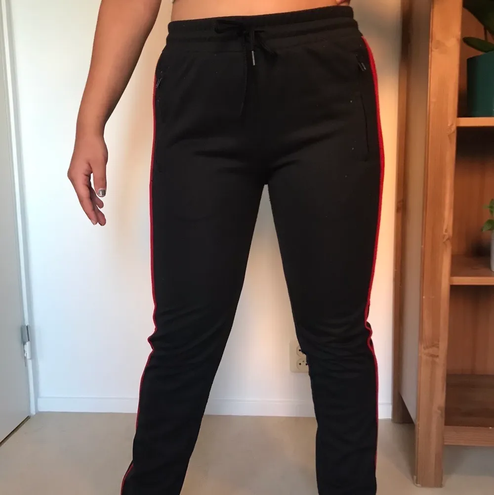 Svarta mjukisbyxor med en röda rämnar längs benen och även resårband nertill. Endast använd . Jeans & Byxor.