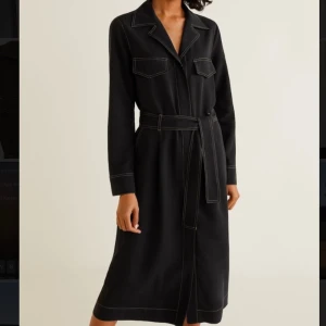 Svart långärmad skjortklänning - Väldigt snygg kläning med bra kvalité på materialet. Knappar framtill längst hela så man kan välja hur mycket slits man vill ha. Knyter med band i midjan