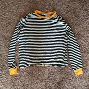 Svart-vitrandig tröka - Randig tröja med gula detaljer. Gott skick.