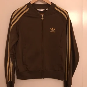  - Snygg brun-guldig retro adidas tröja. Väldigt fin i skick för att vara några år. Lite noppig om man kollar nära, men inget man ser på håll. Det är storlek 38, men den är ganska liten i storlek.. så det beror ju på om man vill att den ska sitta tight eller löst.   Kan skickas mot frakt. 