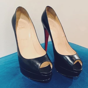 Christian Louboutin ”Lady Peep” strl 40 - Platåpumps i svart skinn med peeptoe, "Lady Peep" köpta på Bukowskis men tyvärr en storlek för stora. Röd sula, märkta "Christian Louboutin Paris". Klackhöjd 15 cm.  Med dustbags. I originalkartong. Ställvis slitage.