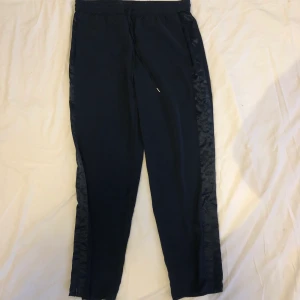 Mörkblå kostymbyxor - Mörkblå kostymbyxor i något tunnare material, rak i benen. Siden remsa på sidorna med diskret dragkedja som man kan dra upp ifall man vill ha slits. Köpt från H&M, aldrig använda, strl 42 (men passar 38-40 också beroende på hur man vill att de ska sitta. Köparen står för frakten :)