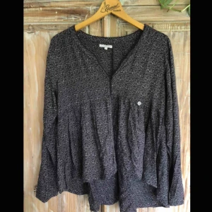  - Svart blus med blomliknande vita detaljer. Väldigt mjuk och faller fint, med knappar längst ner på ärmarna och tre knappar längst fram. Broderi på kanterna. Fint skick.