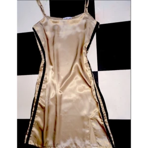  - Miniklänning från Omighty, champagnefärgad med två svarta streck på sidan. Aldrig använd, endast provad hemma. Lappen kvar. Måste tyvärr sälja då den var för liten/inte satt bra på mig. Den är M, men känns snarare som en liten S.