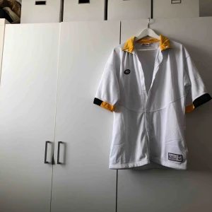  - Häftig t-shirt med knappar. Köpt på secondhand. Finns två små fläckar längst ner på t-shirten. Inte vart ett problem för mig då jag stoppat ner den sidan i byxan vid användning