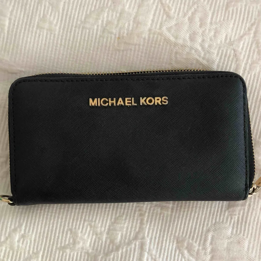 Äkta Michael kors plånbok med plats för kort, pengar och mobiltelefon. Använd men i fint skick. Remmen man kan ha runt handen är tyvärr borta därav det billiga priset. . Accessoarer.