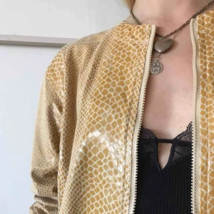  - Gul/beige jacka i glansigt ormskinnsmönster, dragkedja och fickor 