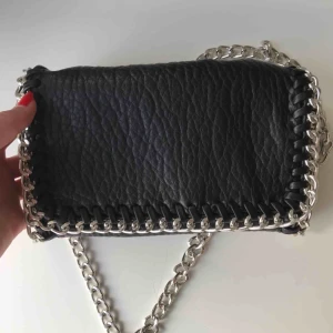  - Priscilla, axelremsväska från Tiamo, väskan är i skinnimitation med silverdetaljer, det finns fack med dragkedja på både baksidan och insidan av väskan. Sparsamt använd och frakten ingår i priset.