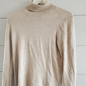  - Beige polotröja med guldiga knappar längst slutet av armen. 