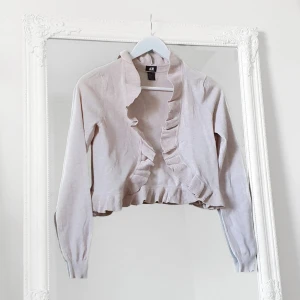 Beige kofta XS volang - Färg: beige.  Strl: XS.   Fin kofta från H&M. Så gott som ny, använd vid ett tillfälle. Detaljer av volang och slaglikande fall framtill. Fint skick! Frakt tillkommer, betalning via swish.