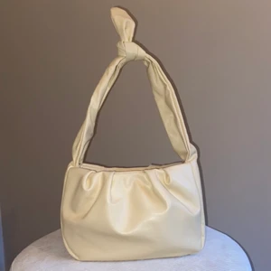 Beige axelväska  - Beige axelväska med skin imitation. Bandet är justerbart i och med knuten som kan knytas upp. Aldrig använd så super fint skick. Rymlig för sin storlek samt en liten innerficka.