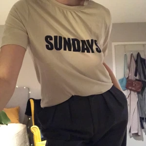 Ljusbeige topp med svart SUNDAYS tryck - T-shirt i sammet-ish. Mycket kortare ”strån” än sammet. Hänger fint på kroppen. Fint skick. Oversized S