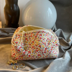 Småblommig necessär - Småblommig röd/gul necessär med blommigt yttertyg,ett vitt mellantyg(syns inte)och gul rutigt/randigt innertyg. Ca 19cm lång,11cm bred och 10 cm hög. Jag hobbysyr bara så kan inte lova raka sömmar eller 100% felfritt. Skickas med frimärke: 22kr och filmar när den skickas. Är din för 100kr plus porto