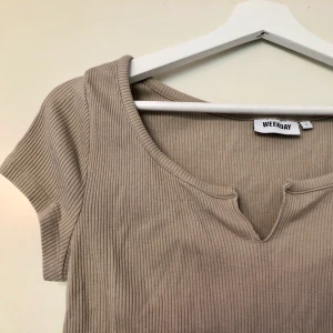 Beige topp med ”slit” från weekday - Beige topp med ”slit” från Weekday. I storlek S men passar nog M bättre. Köpt här på Plick och säljs billigt pga aningen töjd! Frakt tillkommer🍃