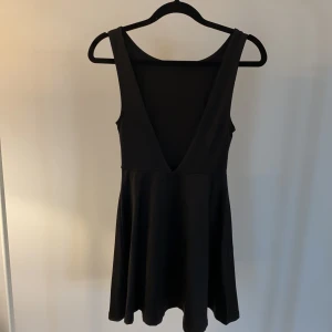 Svart klänning med öppen rygg  - Klänning i stretchig elastan (ungefär bikinityg) med öppen v-ringning i ryggen. Jättefin passform! Från H&M i nyskick 