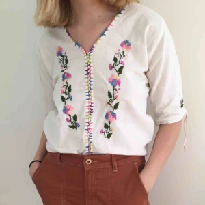  - Superfin blus köpt second hand med broderade blommor i rosa/lila/blåa/gröna/gula toner. Med snörning där fram i samma färgskala. I bomull.