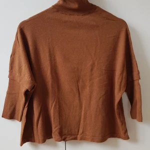 Rodebjer - polotröja - Tunnstickad brun polotröja med ljusblå detalj vid halsen. 60% ull, 30% silke, 10% cashmere. Mycket bra skick, använd en gång. Normal strl. M.