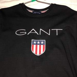 Äkta Gant hoodie utan luva med färgen svart. 50kr om man vill ha påsen med. Priset kan diskuteras (Köper du orginala priset så får du påsen gratis. Lägger till prislappen i de också gratis) Helt ny