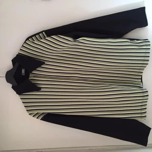 Randig jacka/skjorta med krage - Säljer denna balla och unika skjortan med dragkedja. Den går jättebra att vika in och använda som en jacka eller ha den öppen över en tröja. Ränderna är lila, svart, vit och lila. Baksidan är svårt. Skicket är jättebra! ❤