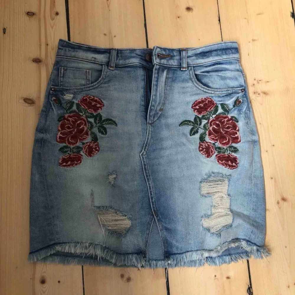 Jättefin jeanskjol från zara i jättebra skick! Det är storlek 34 och är jeansblå med röda detaljer av blommor och konstgjorda slitningar! Frakt: 60kr. Kjolar.