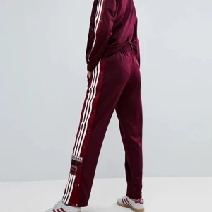 Adidas trackpants - Mörkröda Adidas trackpants i storlek S/36. Knappar längs sidorna. Inköpta för 600 och endast använda ett fåtal gånger