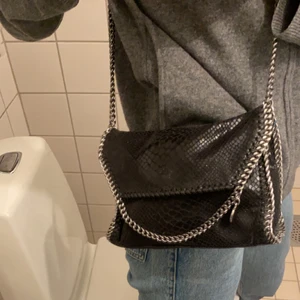 Stella Mccartney Falabells mini - Crossbody väska i svart ”ormskinn”. Svart konstläder och silvrig kedja med snap stängning. Köpt för ett par år sedan men i bra skick. Perfekt handväska där du får plats med det nödvändiga i. Nypris 6800. Pris kan diskuteras