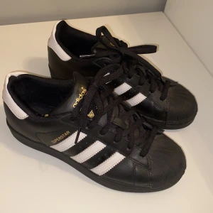 Adidas superstar svarta skor - Svarta adidas skor superstar , använd max fyra ggr så i mycket bra skick! Ny pris (700 kr) och jag säljer dom för 250 ,säljaren står för frakt! Vid snabb affär kan priset sänkas! 