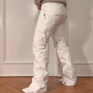  - Vita snowboard/skidbyxor från Burton. Resår för anpassning av midjestorlek. Fodrade och med dragkedjor för ventilation. Aningen slitna längst ner i benen samt en liten fläck där jackan brukar hänga över i bak (se sista bilden). Annars i fint skick. 