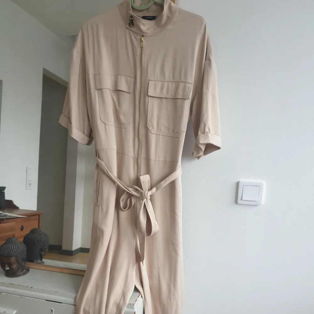 Snygg beige jumpsuit byxdress från Lindex. aldrig använd! bara provat. storlek s men sitter oversized. fickor på framsidan och baksidan. Med knytband. Kan skickas annars finns i Malmö! Frakt ingår . Övrigt.