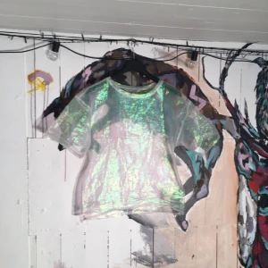  - En see-through cool Tshirt som skimrar i olika färger. Strl S men är stor och fyrkantig i passformen. Snygg att ha över sina kläder tex en topp/snygg BH under. Bara provad. Lapparna är bortklippta för att inte ska synas igenom. Köparen står för frakten.