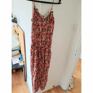  - Somrig jumpsuit med knappar och snörning i midjan. Inköpt second hand. Mycket bra skick. Skickas mot portokostnad. 