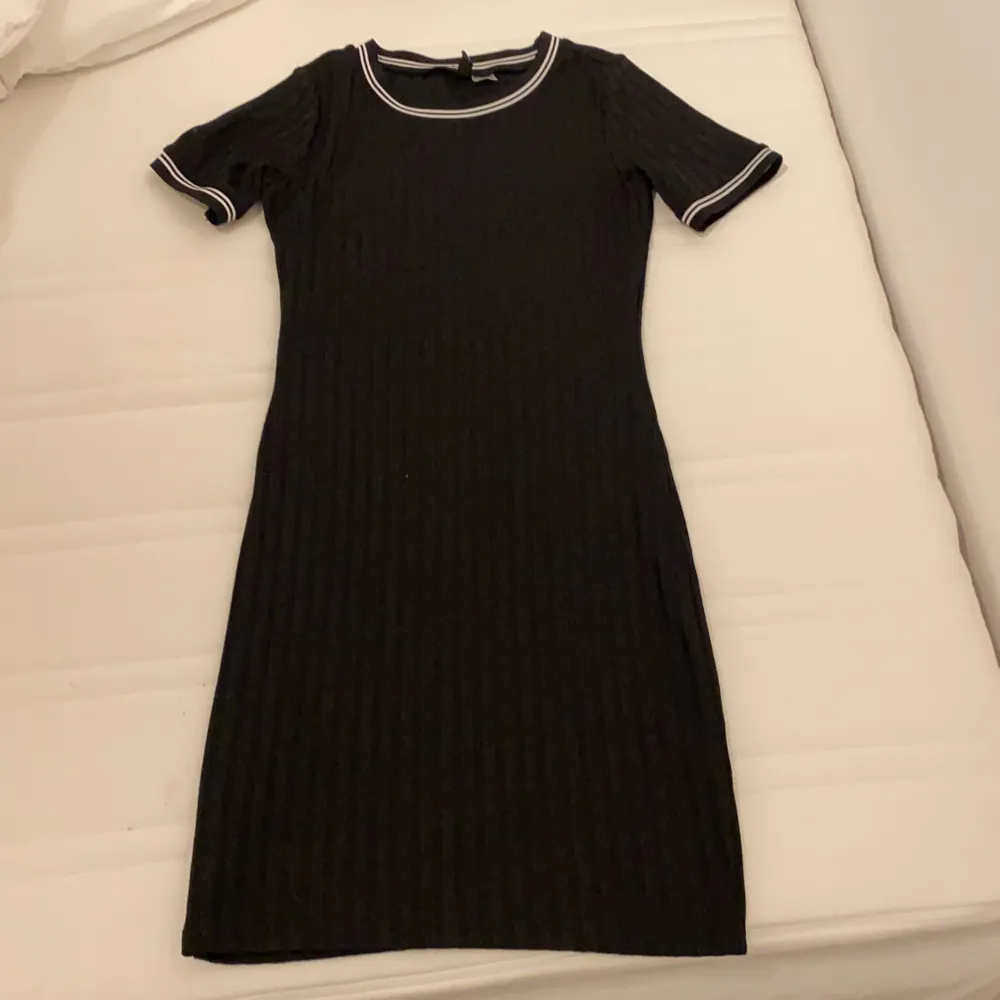 En vanlig svart klänning med vita sträck vid armarna och halsen. Klänningar.