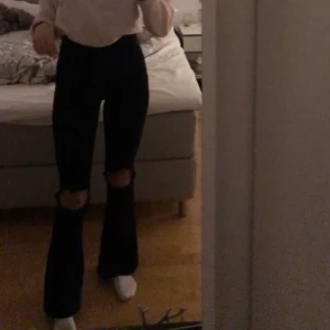 svarta bootcutjeans med hål - Säljer dessa svarta bootcutjeans med hål på knäna, skitbra passform verkligen! De är stretchiga i materialet så de formar sig fint på kroppen 🥰 strl 34 och frakten är ej inkluderad i priset