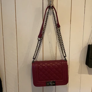 Axelbands väska - Axelremsväska som inte kommer till användning. Färgen är vinröd/mörkrosa. Man får plats med väldigt mycket i den. 