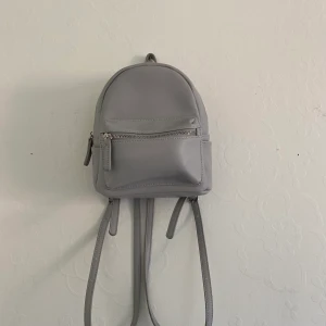 Grå Mini ryggsäck - Grå mini ryggsäck i bra skick från Forever 21. Funkar utmärkt men fick inte tillräckligt bra användning som jag trott. Köpare står för frakt.
