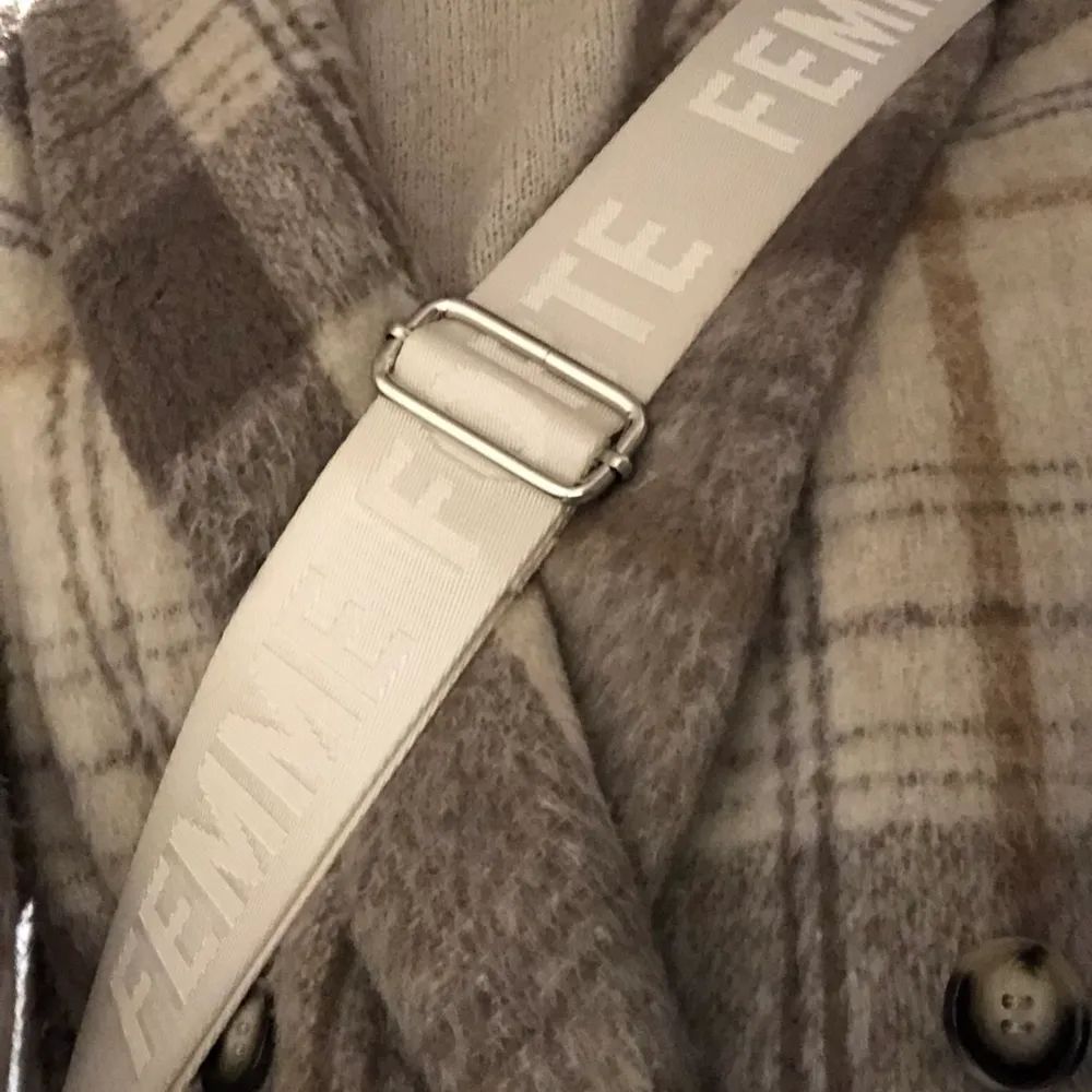 Supersnygg väskrem med texten ”Femme Forte”, remmen är i en vit/beige/silvrig färg som passar väldigt bra till de flesta basfärgerna!!. Accessoarer.