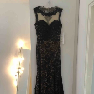  - Svart balklänning i spets med superfina detaljer i rygg och över bröstet. Slits i sidan. Kontakta mig för fler bilder!   Nypris 4800kr. Aldrig använd, alla lappar är kvar.  Köparen står för frakt. 