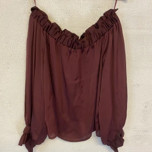 Off Shoulder blus - Blus med bara axlar i en mörk vinröd färg. Fina volanger och sitter fint. Mycket fint skick och är i storlek M. 80kr och köparen står för frakten.