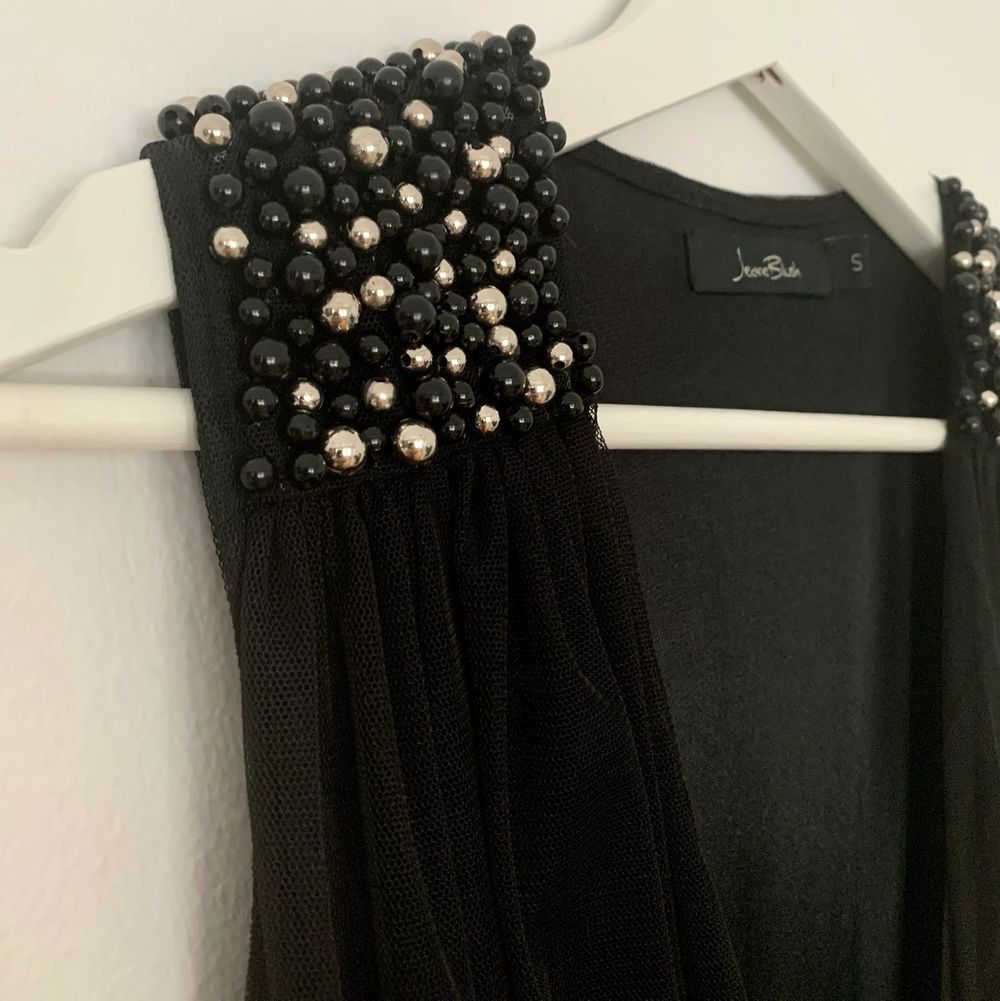 Helt ny festklänning från märket Jeane Blush, som tyvärr inte kommit till användning. Klänningens axlar pryds av vita och svarta pärlor. Klänningen stängs med en diskret dragkedja på sidan i midjan. Klänningen har en rätt djup v-ringning. Storlek S. . Klänningar.