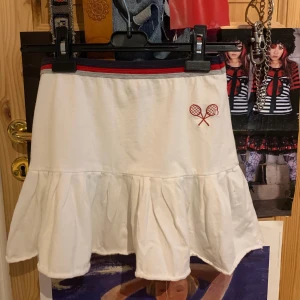 Tennis Kjol Vit Blå Röd Grå - supersöt tenniskjol med broderade tennisrack! funkar både som highwaist och lowwaist. rekommenderar ljusa underkläder, tyget är lite tunnt men inte genomskinligt. 35cm lång, 32cm i midjan när den ligger ner, men har resår