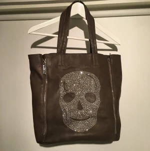  - Mörkgrå väska med dödskalle i strass och dragkedjor på sidorna.