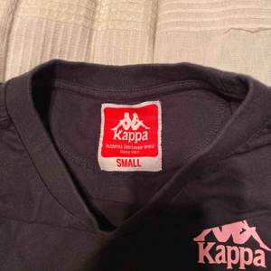 Svart Kappa T-shirt i fint skick i storlek S. Säljs pga använder aldrig. Ljus rosa tryck på vänster bröst samt rygg
