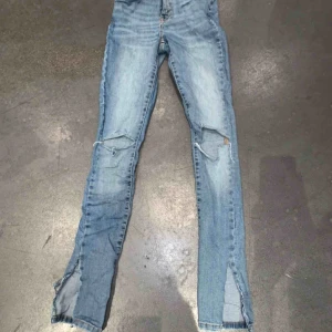 Blåa jeans med slits och hål - Ett par asballa ljusblåa jeans med både slits och hål vid knäna. Ett av mina favorit jeans. Passar xs/s. Väldigt bra skick. Köparen står för frakten 