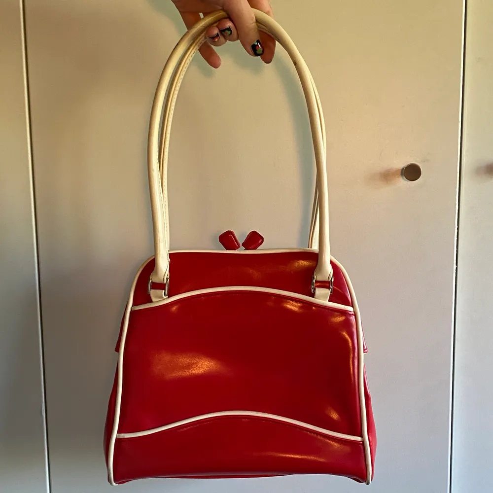 Röd väska i retro-stil. Den är glansig med metallförslutelse som man knäpper ihop. Lite sliten men fortafarande fräsch. Säljer på grund av att den inte passar min stil längre. Frakt 63kr. Väskor.