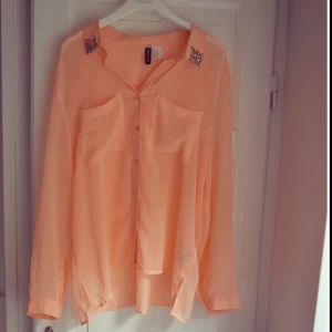  - Aprikosfärgad blus med dekorerade kragar. Perfekt att bära på varma sommardagar eller slarvigt nerstoppad i jeansshorts. Själv har jag använt den som oversize blus!