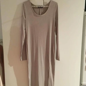  - Grå/beige ribbad, tajt klänning med slits. Ursprungligen från Nelly. Aldrig använd! Storleken passar även något större och något mindre tack vare stretchen! Köparen står för frakten.