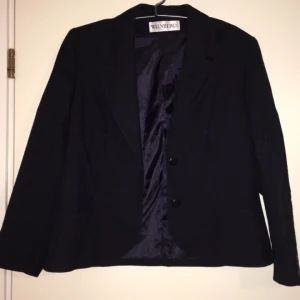  - Kavaj med axelvaddar för att ge mer struktur. Tyget är strävt, liknar linnetyg fast inte riktigt och är i färgen svart/marinblått