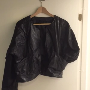  - Svart läderjacka av märket Hollies. Lite Grease-känsla med virkade detaljer på ärmarna. Liten vit fläck på magen som går att täcka bort eller ha som den är. Ball fit, men tyvärr lite för stor!