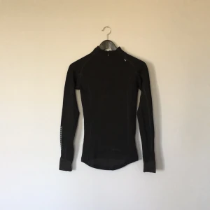  - Warm underställströja i svart från Helly Hansen. Syntetmaterial på insidan av tröjan och merinoull på utsidan. Halv-zip dragkedja för extra värmande effekt och smidigare användning. Först till kvarn!