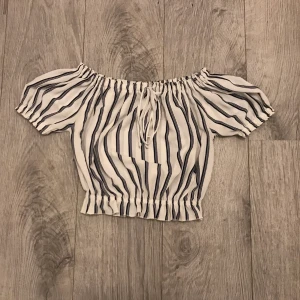 Vit och svart randig off shoulder crop top - Vit och svart randig off shoulder crop top med snöre i mitten. Bra kvalité, storlek XS-S. Vid intresse kan eventuellt fler bilder skickas.